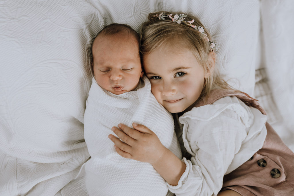 big sister and baby on white pillows lifestyle shoot