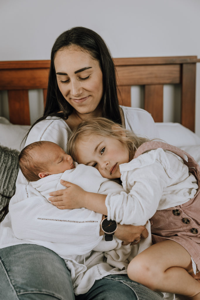 baby being held by mum on a bed and sister cuddling them