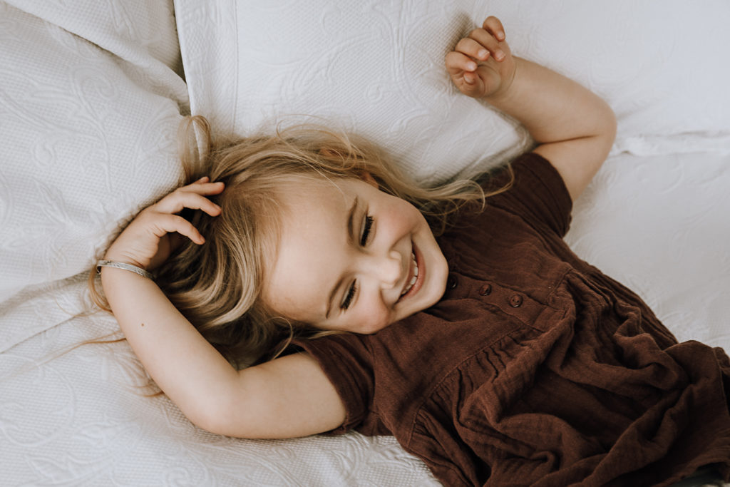 little girl smiling to herself on white pillows