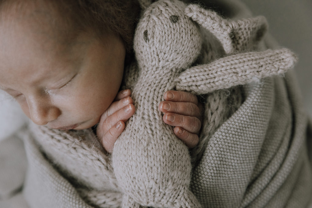 tiny fingers of baby boy holding a beige bunny