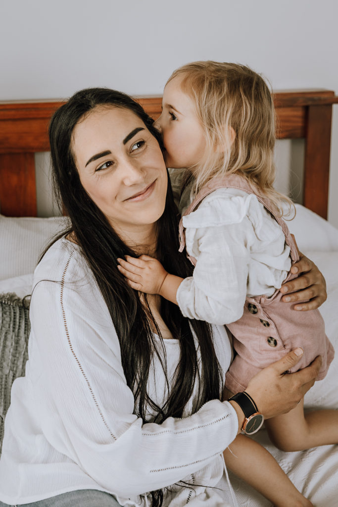 girl telling mum a secret on a white bed