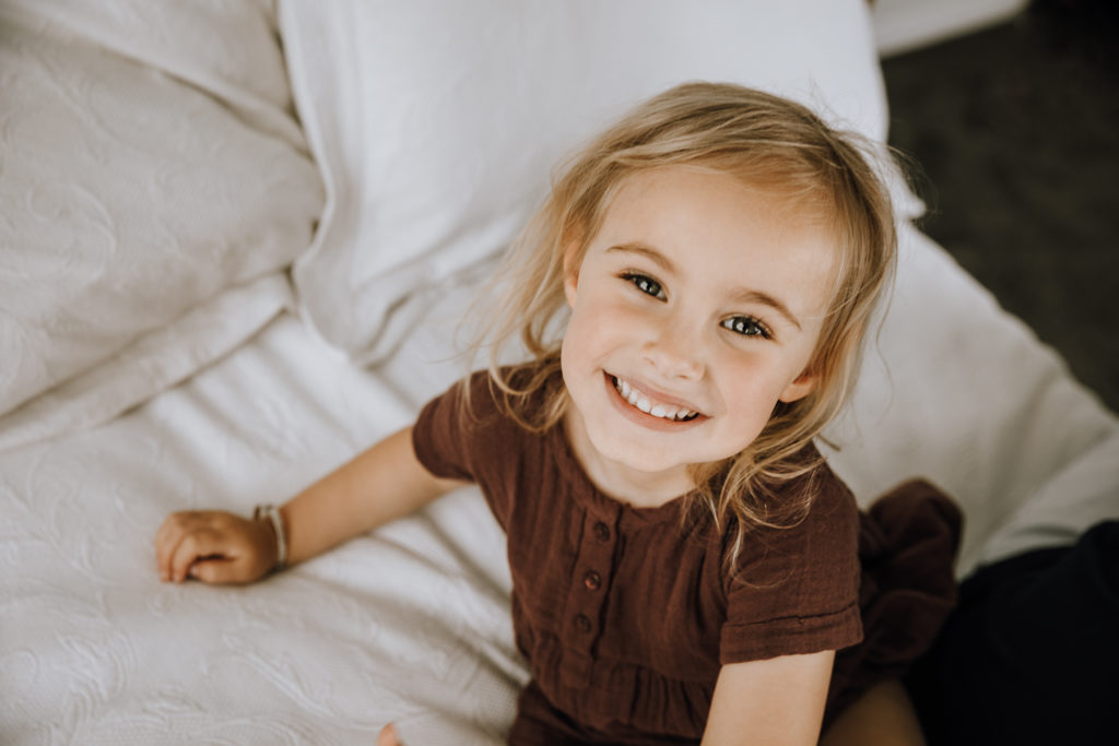 beautiful little girl in brown top smiling at the camera white background