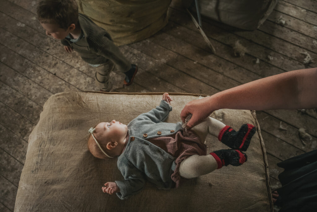 baby girl laying on a wool sack with her brother walking past.