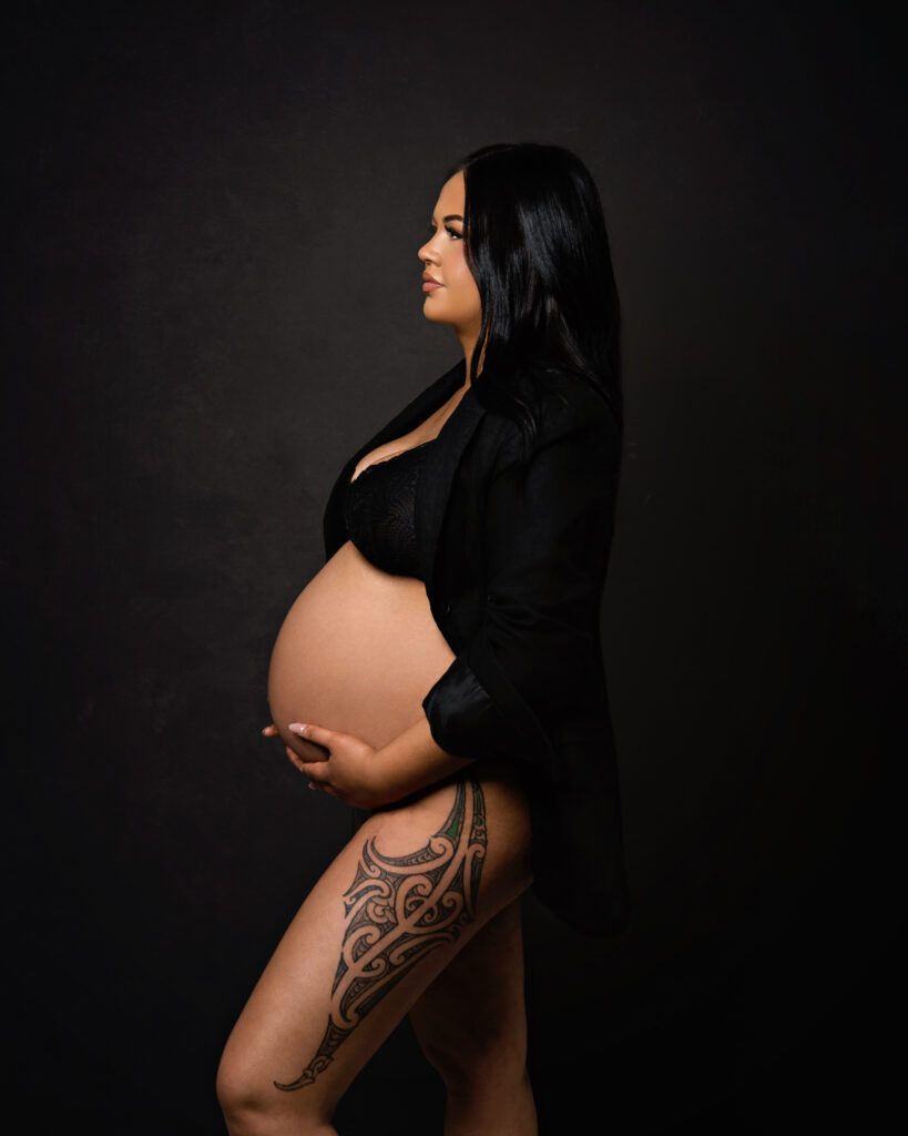 studio portrait pregnant lady with maori tatoo on thigh in black on dark backdrop