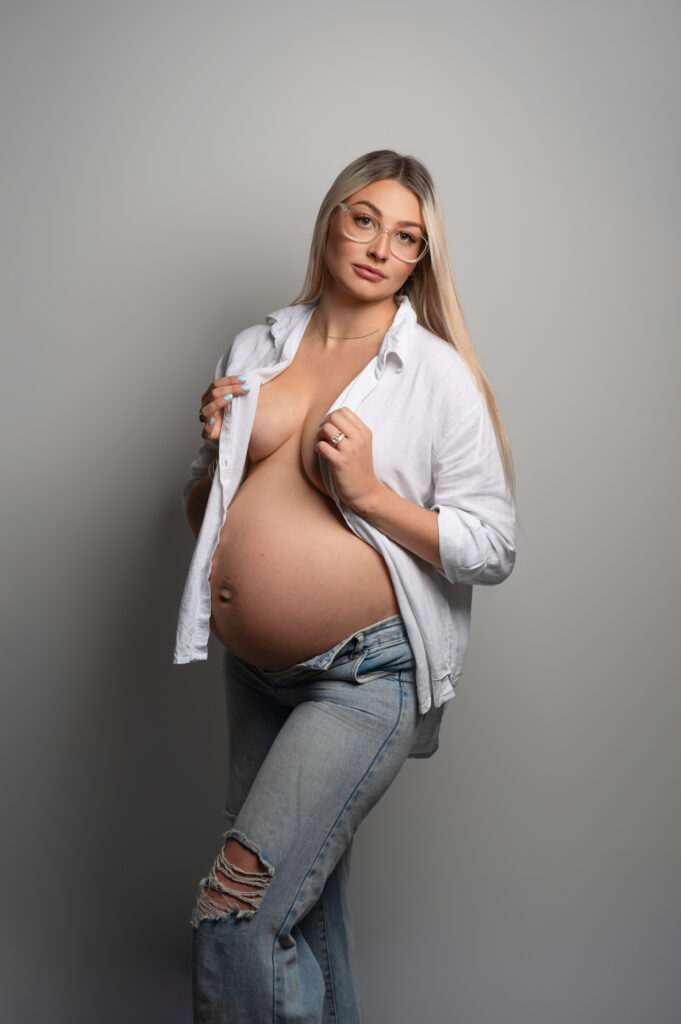 blonde pregnant lady in simple black dress seated infront of an elaborate draping fabric and frame backdrop