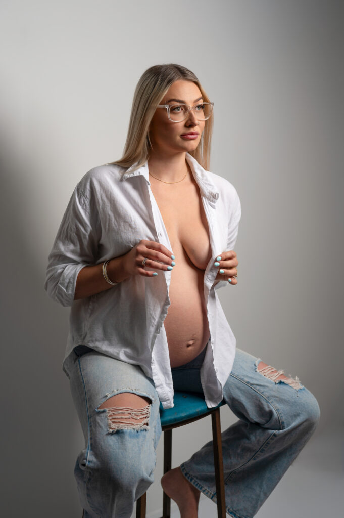 blonde pregnant lady in simple black dress seated infront of an elaborate draping fabric and frame backdrop