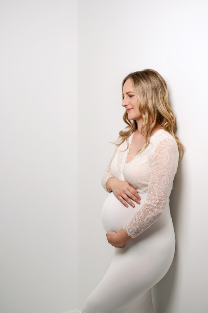 simple cream dress pregnant lady leaning against white studio wall