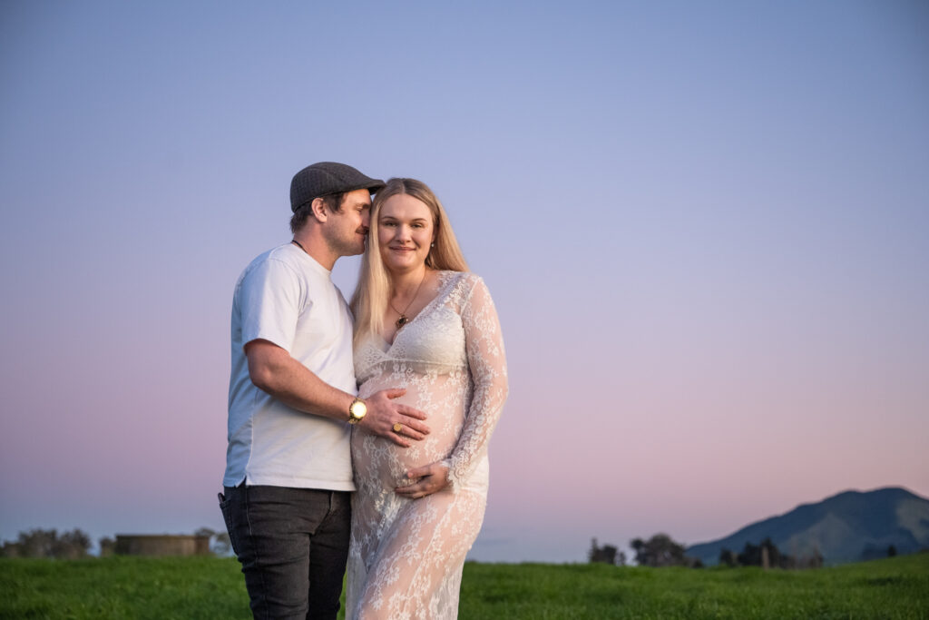 hisband and wide infront of blue purple skies cuddling pregnant belly
