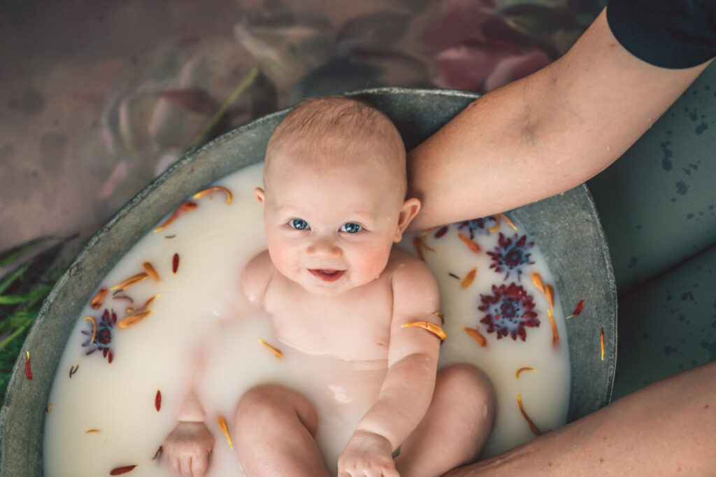 baby girl in milk bath with orange flowers and big smile
