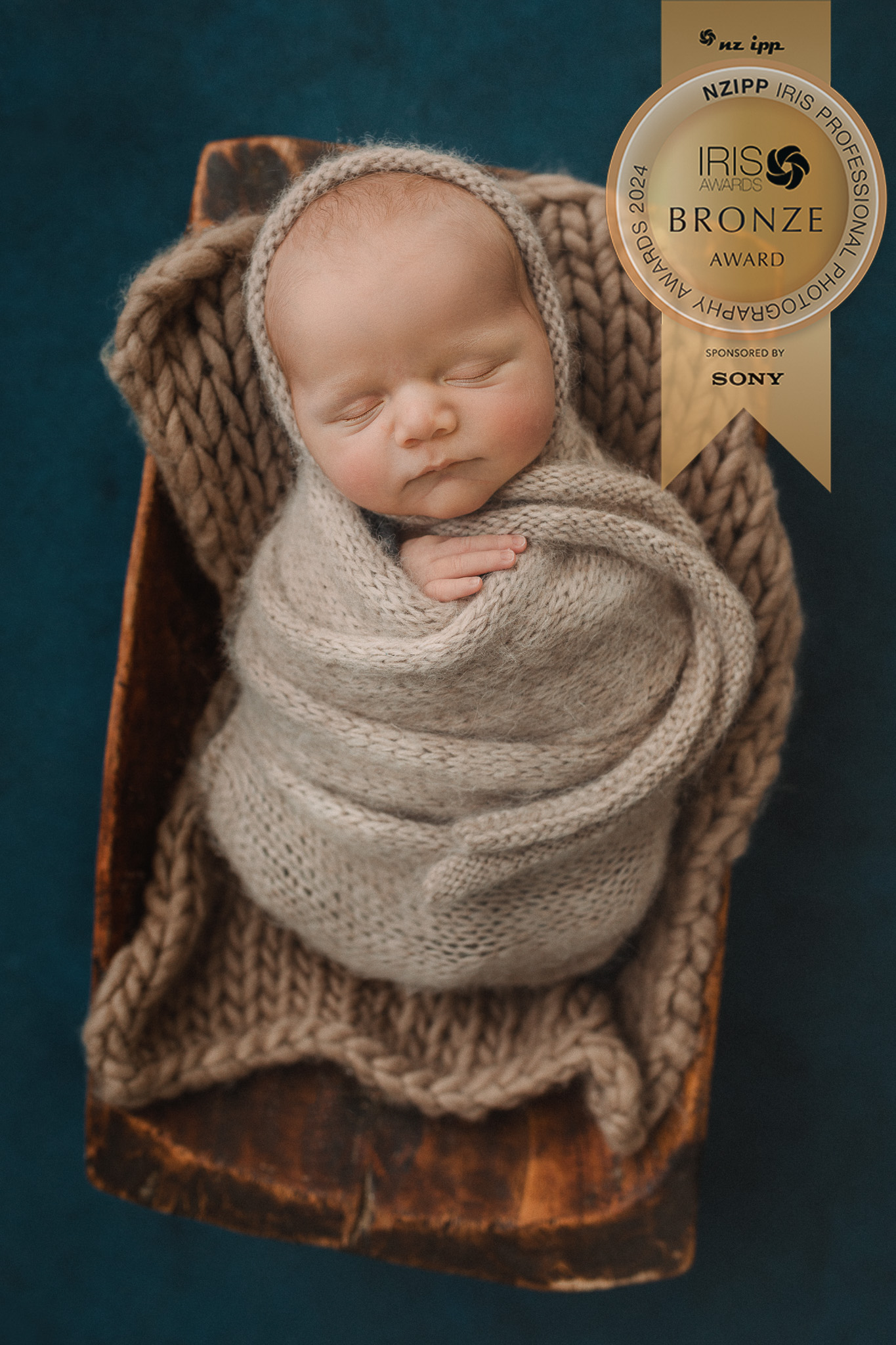 newborn baby boy in beige wrap in trench bowl on blue backdrop