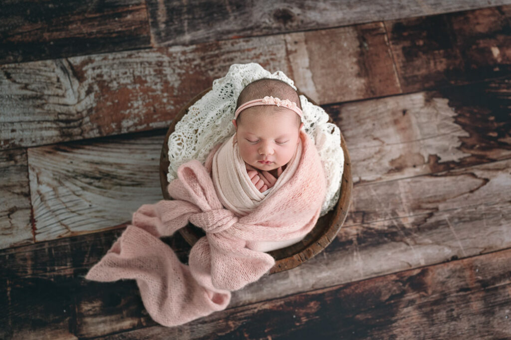 baby girl wrapped in a pink bow, in a wooden bowl.
