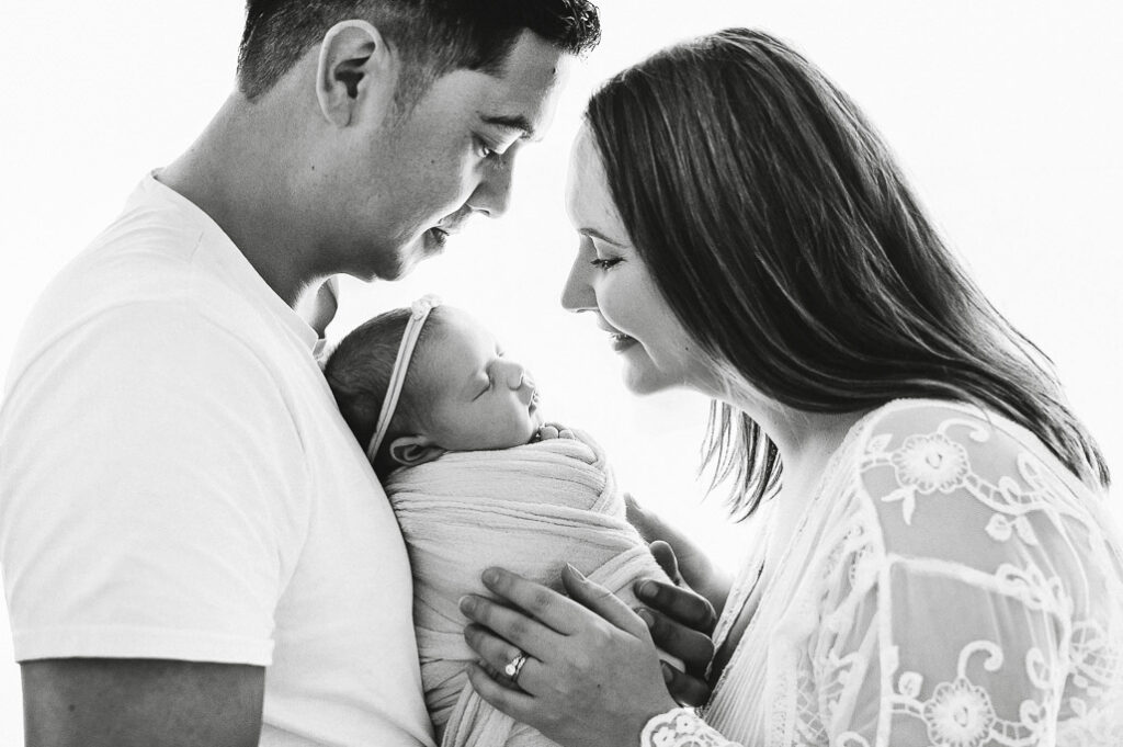 Mum smiling down at her newborn baby girls face, in black and white
 