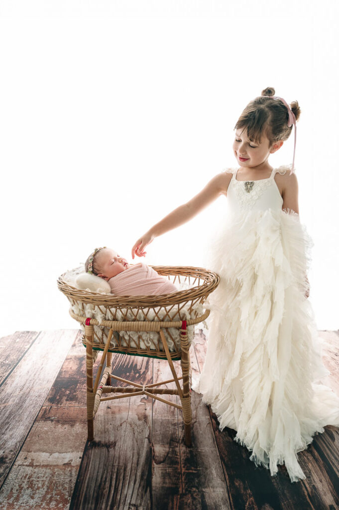 baby in a small bassinet and her beautifully dresses sister beside her 